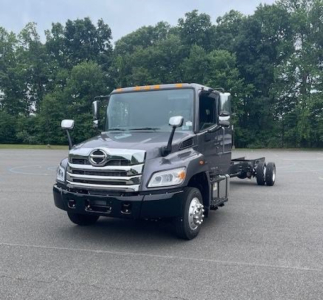 Hino L6 cab chassis truck front view with chrome grille, side mirrors, and orange cab roof marker lights in a parking lot.