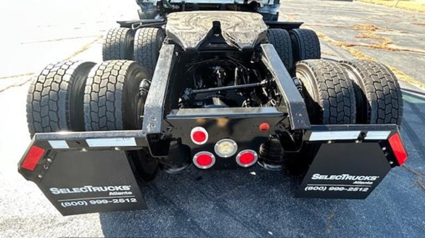 Back of a Freightliner Cascadia chassis with dual rear axles and raised fifth-wheel, showing mud flaps with SelectTrucks branding and center-mounted lights.