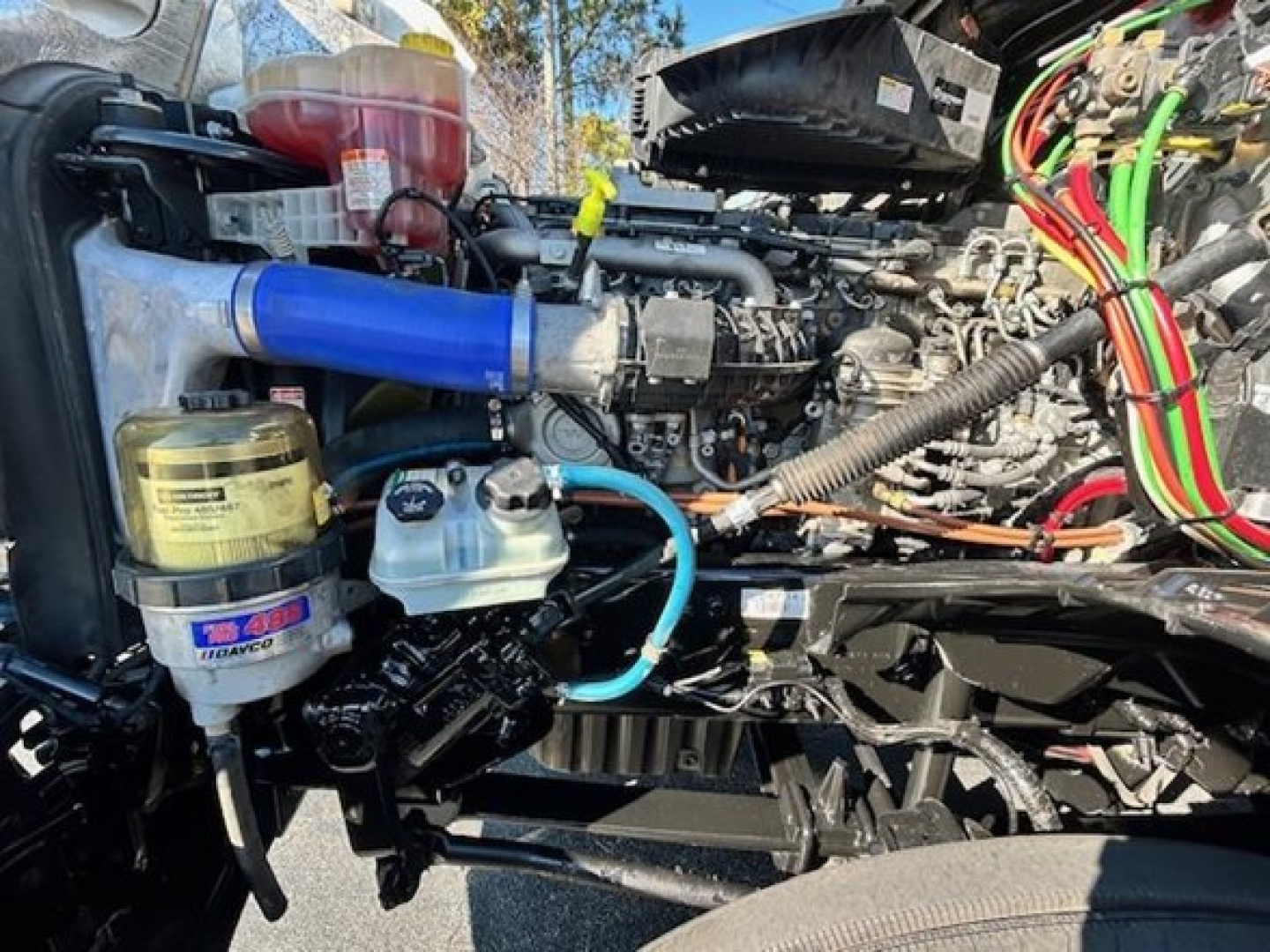 Freightliner Cascadia 126 engine bay showing blue silicone intake hose, coolant reservoir, hydraulic reservoir, and assorted color wiring harnesses.