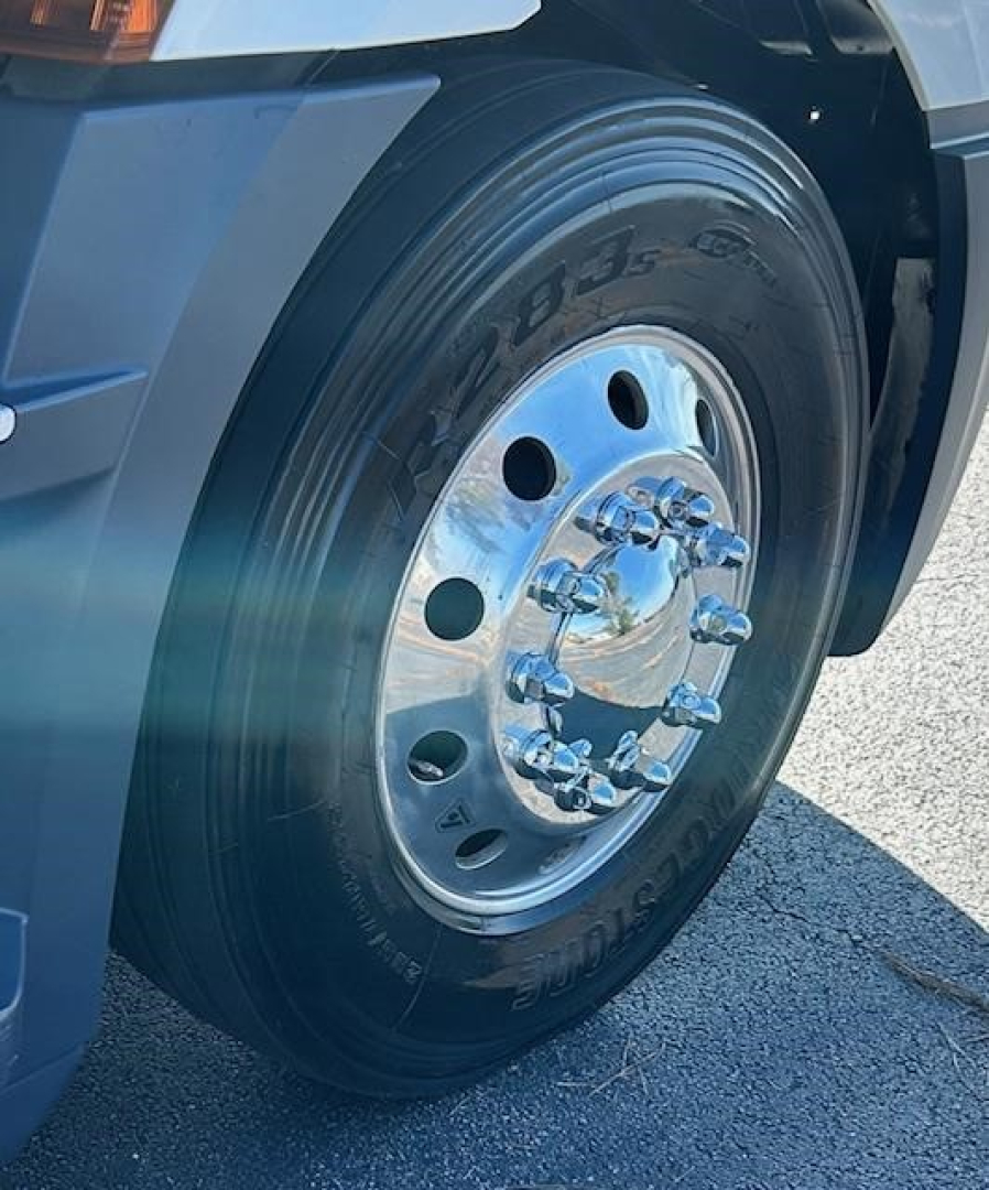 Truck wheel close-up showing steel rim and lug nuts on a Freightliner Cascadia 126 front wheel with tire markings visible.