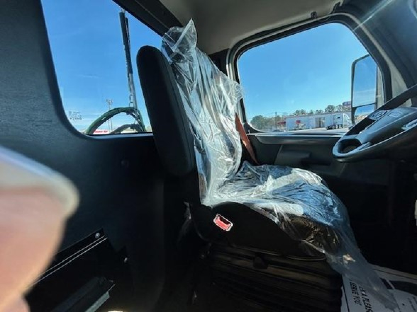 Truck cab interior showing driver seat wrapped in plastic, steering wheel and dashboard visible in Freightliner Cascadia cab.