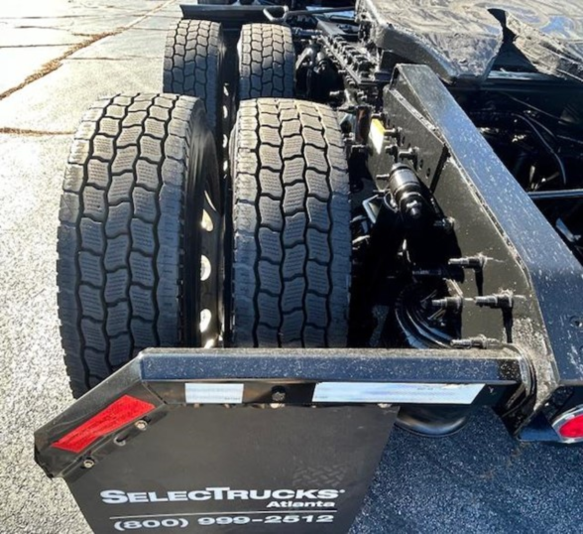 Rear axle pair and chassis of a Freightliner Cascadia day cab showing dual rear wheels, suspension, and frame with SelectTrucks Ariane license plate area.