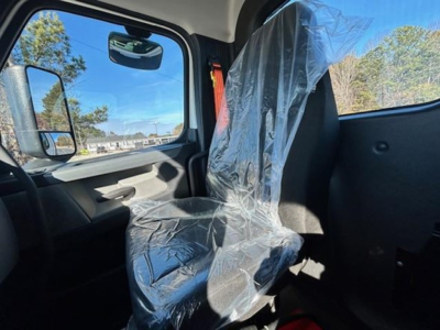 Truck cab interior showing passenger seat wrapped in protective plastic and side window with mirror; blue sky and trees visible outside.