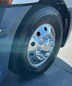Truck wheel close-up showing steel rim and lug nuts on a Freightliner Cascadia 126 front wheel with tire markings visible.