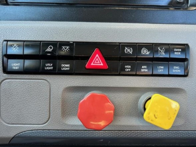 Freightliner Cascadia dash panel with large red hazard button, yellow and red knobs, and multiple function icons visible.
