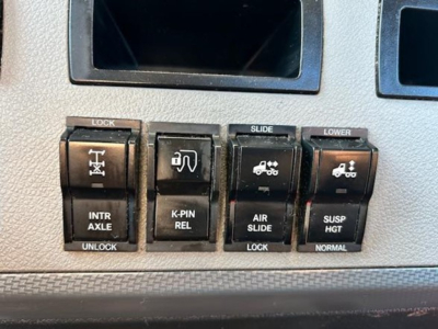 Dashboard switch panel showing lock,Intr Axle, K-PIN rel, air slide, lower suspension controls in a Freightliner Cascadia cabin.