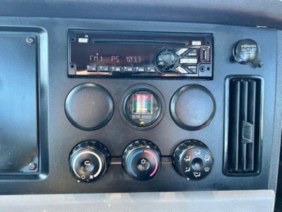 Truck dashboard panel showing climate/auxiliary controls and a single-DIN radio in a Freightliner Cascadia dash with round AC knobs and power outlet