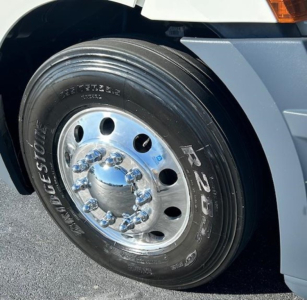 Truck wheel and front fender of a Freightliner Cascadia showing a Bridgestone tire and polished chrome hubcap with lug nuts.