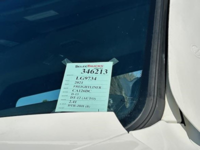 Truck window with a listed sale tag: 'SELECTTRUCKS 346213' and item details including '2021', 'D13', 'D-12 (AUTO)', and other specs visible on the sticker.