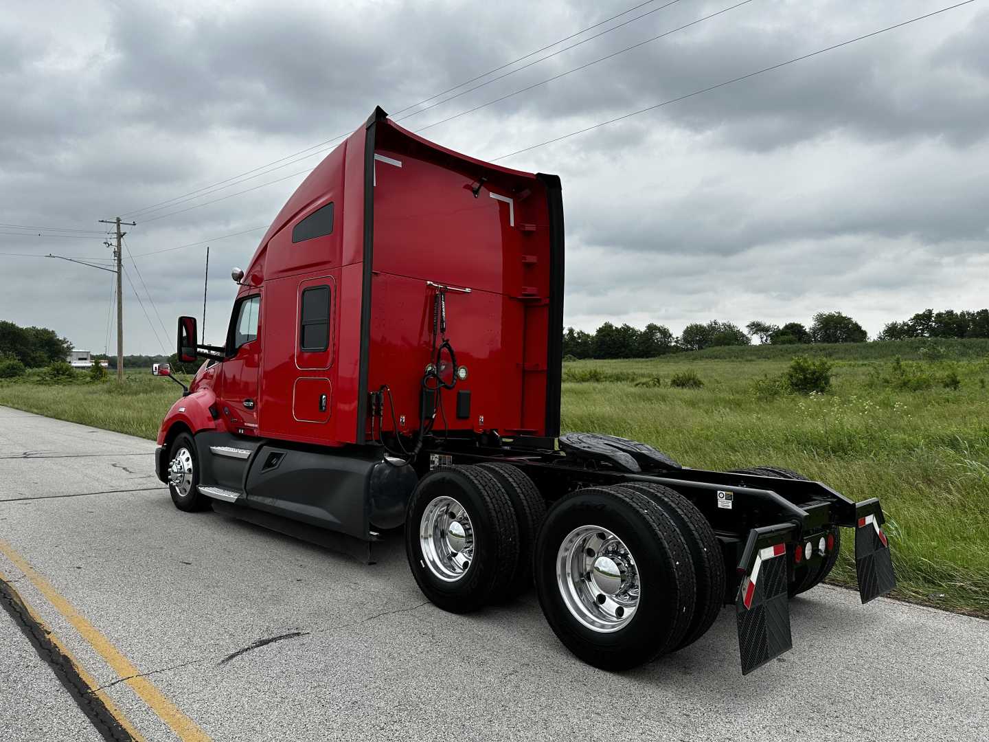 Kenworth T680 tractor in red with sleeper cab, rear view showing dual rear axles and mud flaps