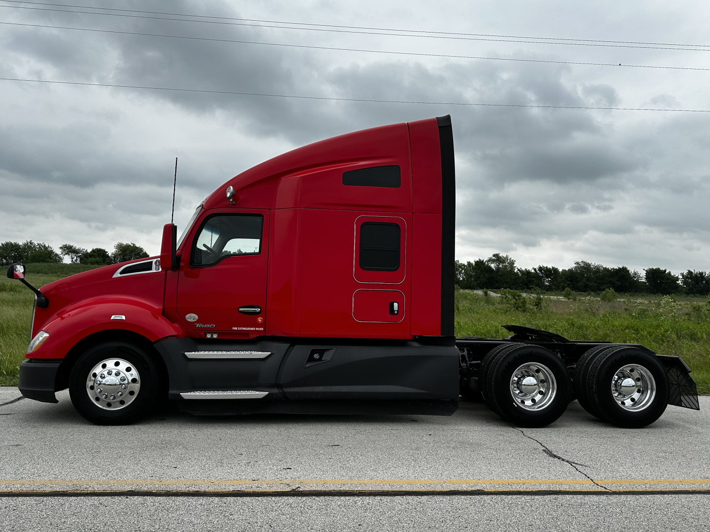 Red 2022 Kenworth T680 conventional sleeper truck side view showing cab profile and rear axles
