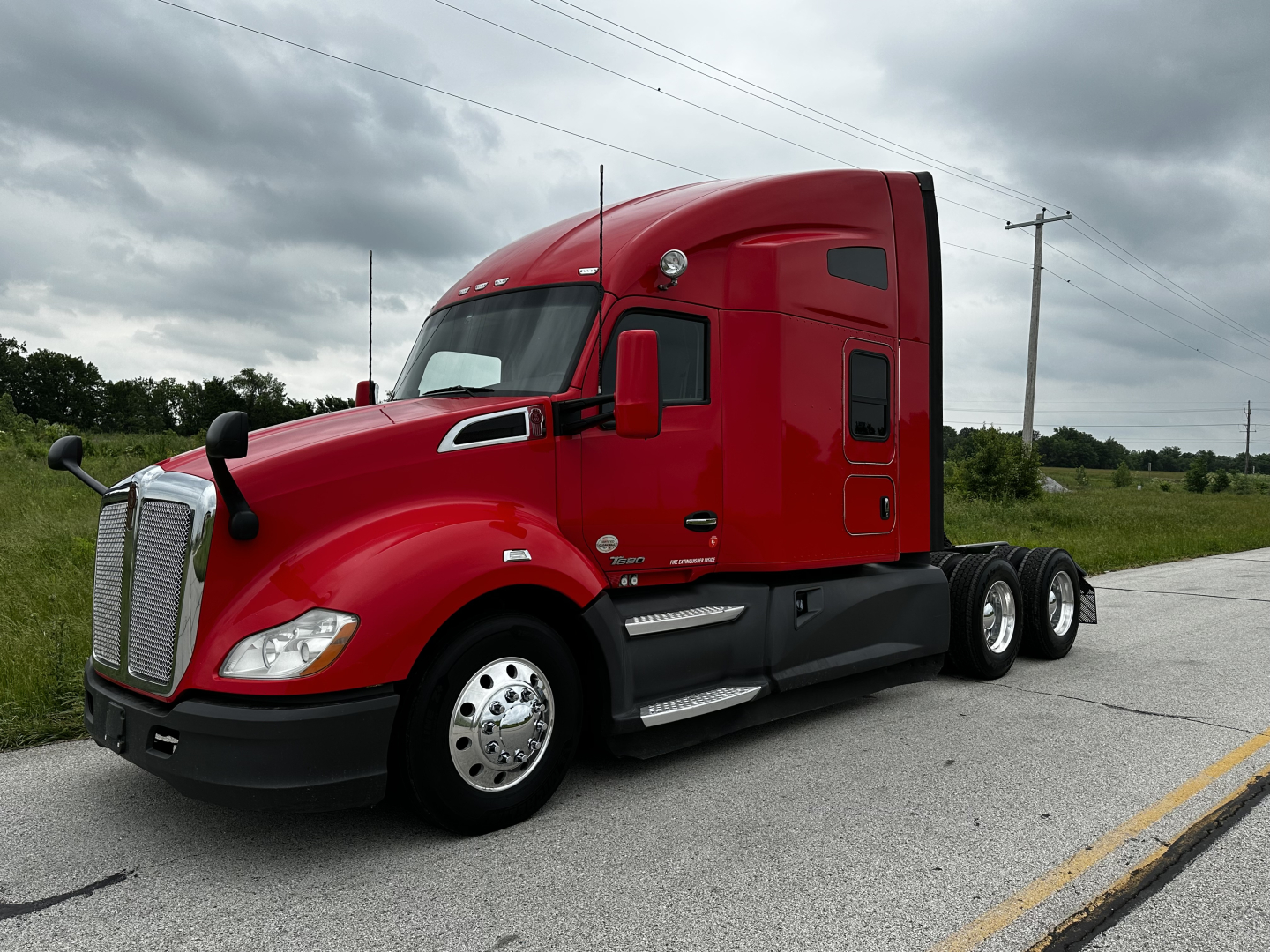 Kenworth T680 tractor in red, front-left view, with sleeper cab and side exhaust; no visible text other than truck features.