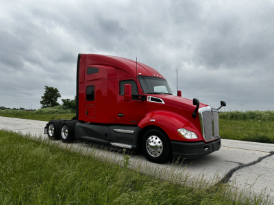 Kenworth T680 conventional sleeper truck in red, side view, on road with clear sky.