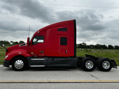 Red 2022 Kenworth T680 conventional sleeper truck side view showing cab profile and rear axles