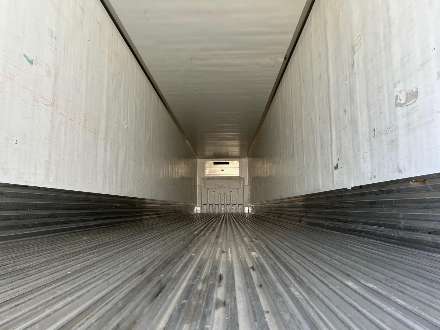 Trailer interior showing empty refrigerated cargo area with ribbed floor and side walls, long perspective toward rear door.