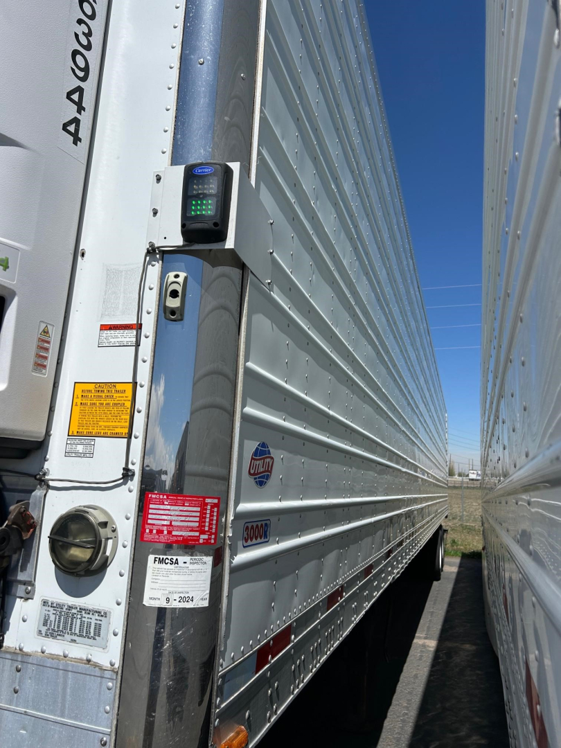 Utility 3000R trailer side and rear door showing a keypad/reader mounted on the door jamb with various stickers and a reflective surface.