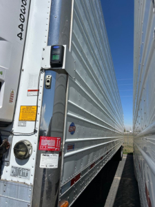 Trailer corner with 2018 Utility 3000R reefer, side entry with scale device mounted on front post, various stickers and safety labels visible.