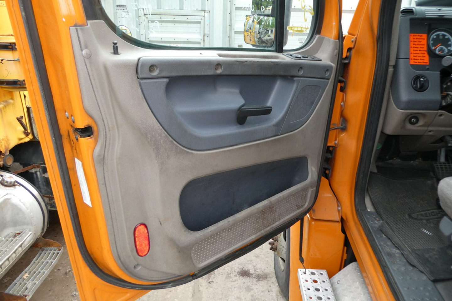 Cab door interior of a 2017 Freightliner Cascadia 125 daycab truck showing orange exterior, gray door panel, window crank, and storage pockets.