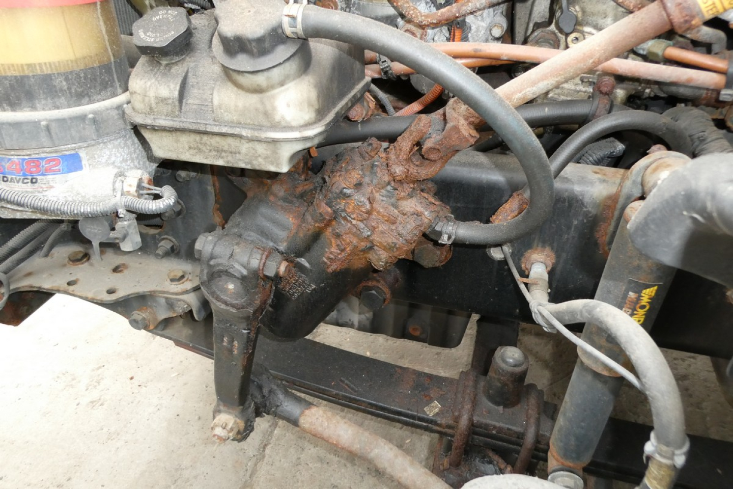 Diesel truck engine bay showing rusted component and hoses in cab-over engine area.