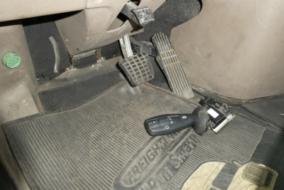Cab area of a Freightliner Cascadia 125 with pedals, steering column, and floor mat showing a key fob and switch.