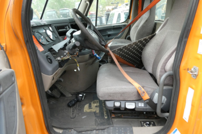 Cab interior of a Freightliner Cascadia 125 daycab showing steering wheel, dashboard, gray seat, and orange exterior door frame.