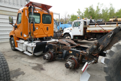 Orange Freightliner Cascadia truck cab with exposed drivetrain sitting in a yard