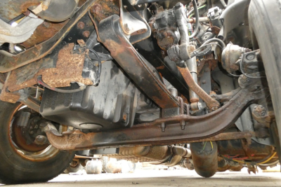Underbelly view of a Freightliner Cascadia 125 truck showing rusted frame, suspension, and exhaust components.