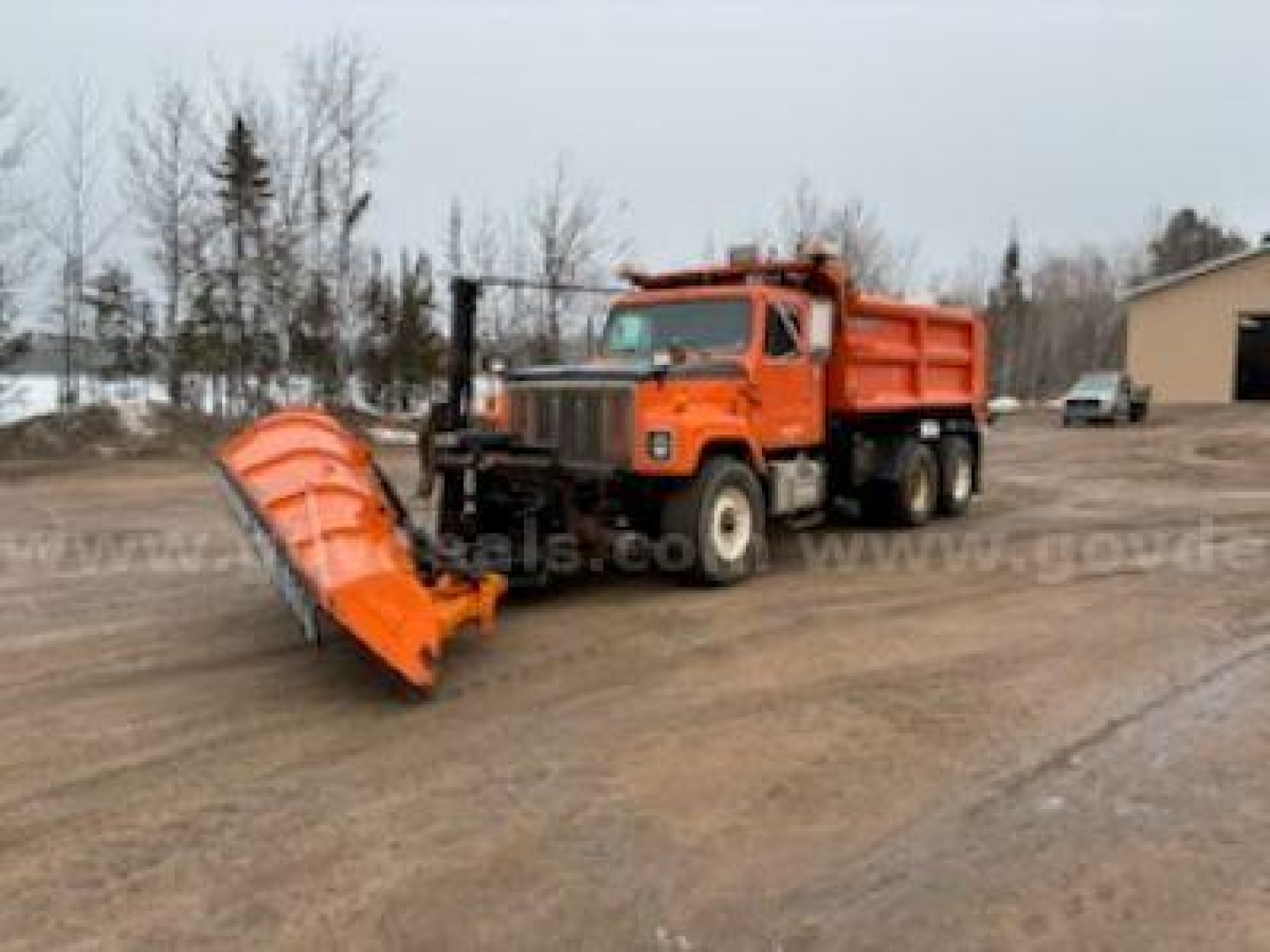1999 International 2574 dump truck with orange snow plow attachment in dirt lot, side view showing dump bed and front wheels.