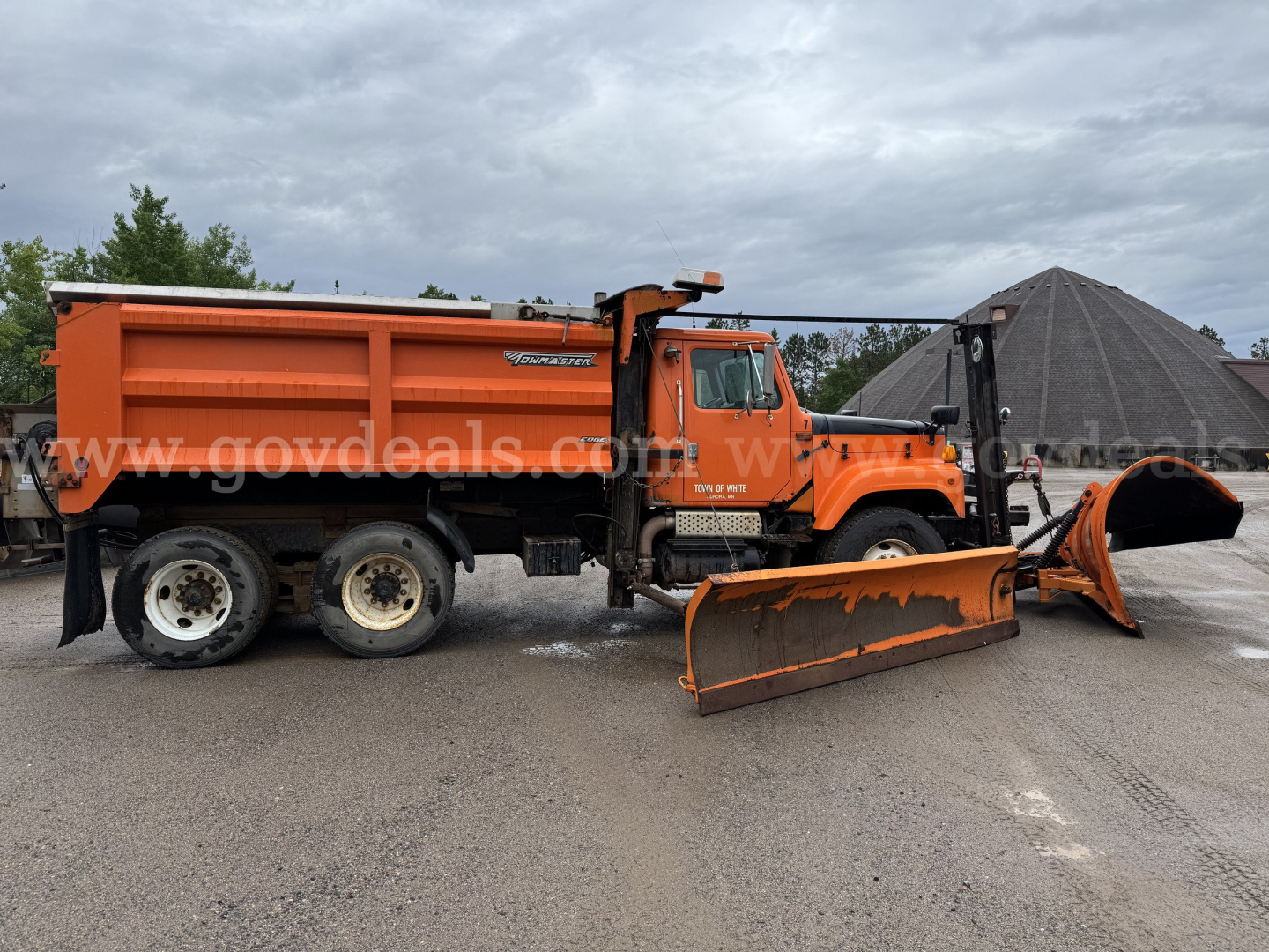 International dump truck in service condition with attached plow and dune-cap snowplow equipment, orange color, side view.