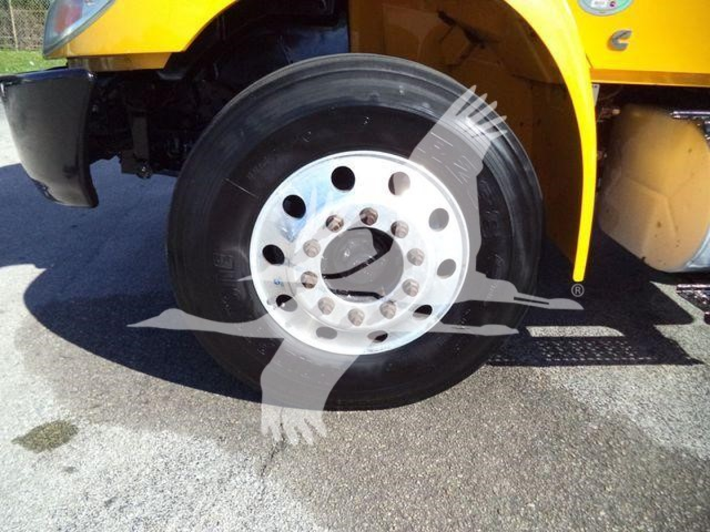 Wheel and front fender of a yellow 2019 International Durastar flatbed truck, showing the front axle with a polished silver multi-hole rim