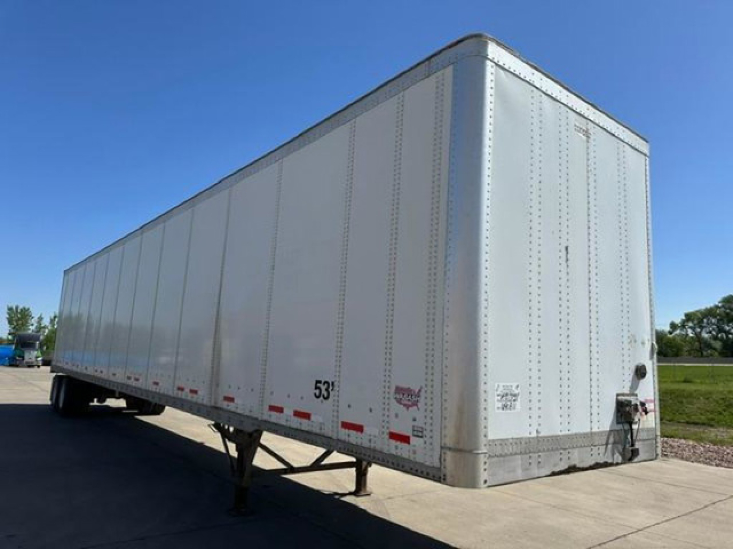 Trailer side view showing a white 53' Wabash van trailer with riveted aluminum body, rear door, and wheel area visible.