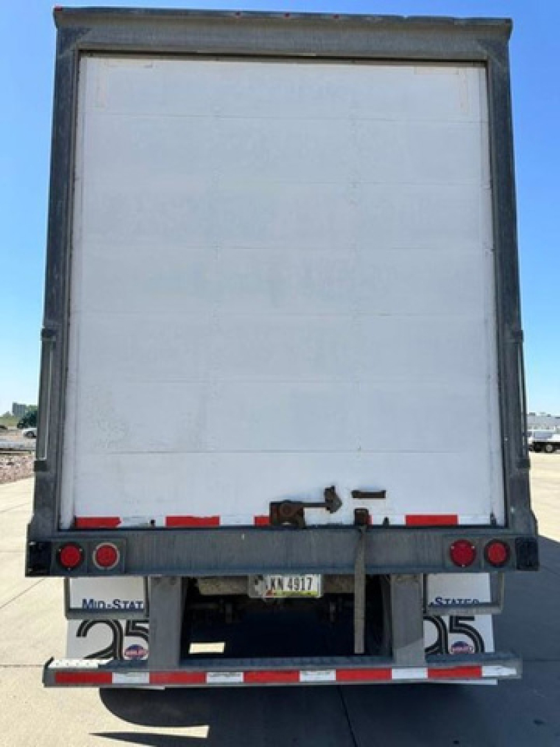 Rear view of a white Wabash trailer with truck under tail lights and bumper. Visible text includes MN-STAT? plates and taillight area.