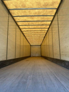 Trailer interior showing long empty cargo space with wooden roof panels and metal side walls.