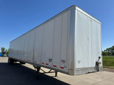 Trailer side view showing a white 53' Wabash van trailer with riveted aluminum body, rear door, and wheel area visible.