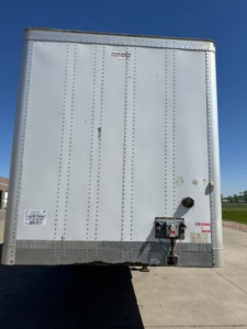 Rear view of a white Wabash trailer with riveted aluminum panels, back doors closed, and hitch/safety chains visible.