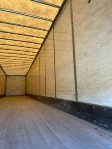 Trailer interior showing empty cargo area with wooden floor and side walls, long rectangular space, roof ribs visible.