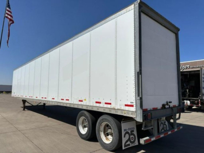 Trailer: white Wabash semi-trailer trailer with dual rear axles, side panel riveted construction, rear doors closed, stock number plate 25, in a dealership lot.