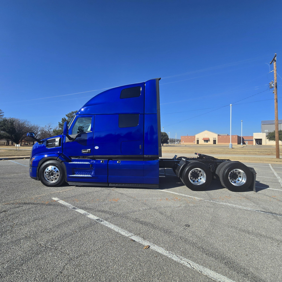 Blue Mack tractor-trailer in a parking lot, side view showing cabin, dual rear axles, low sun glare.