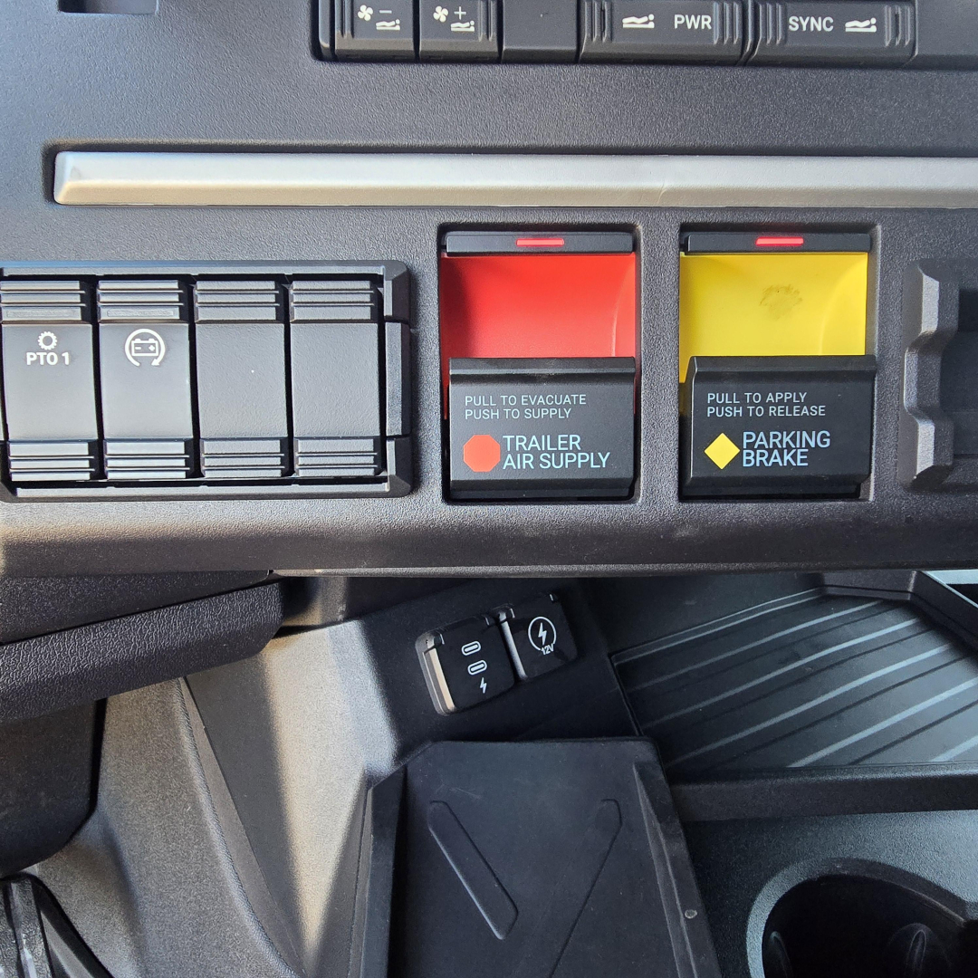 Cab panel with red and yellow tow/warning levers labeled 'Trailer Air Supply' and 'Parking Brake' and various switches, Mack PR64T76H truck interior view.