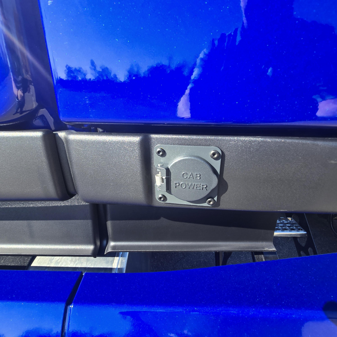 Cab power inlet cover on blue Mack PR64T76H truck showing square plug cover with bolts