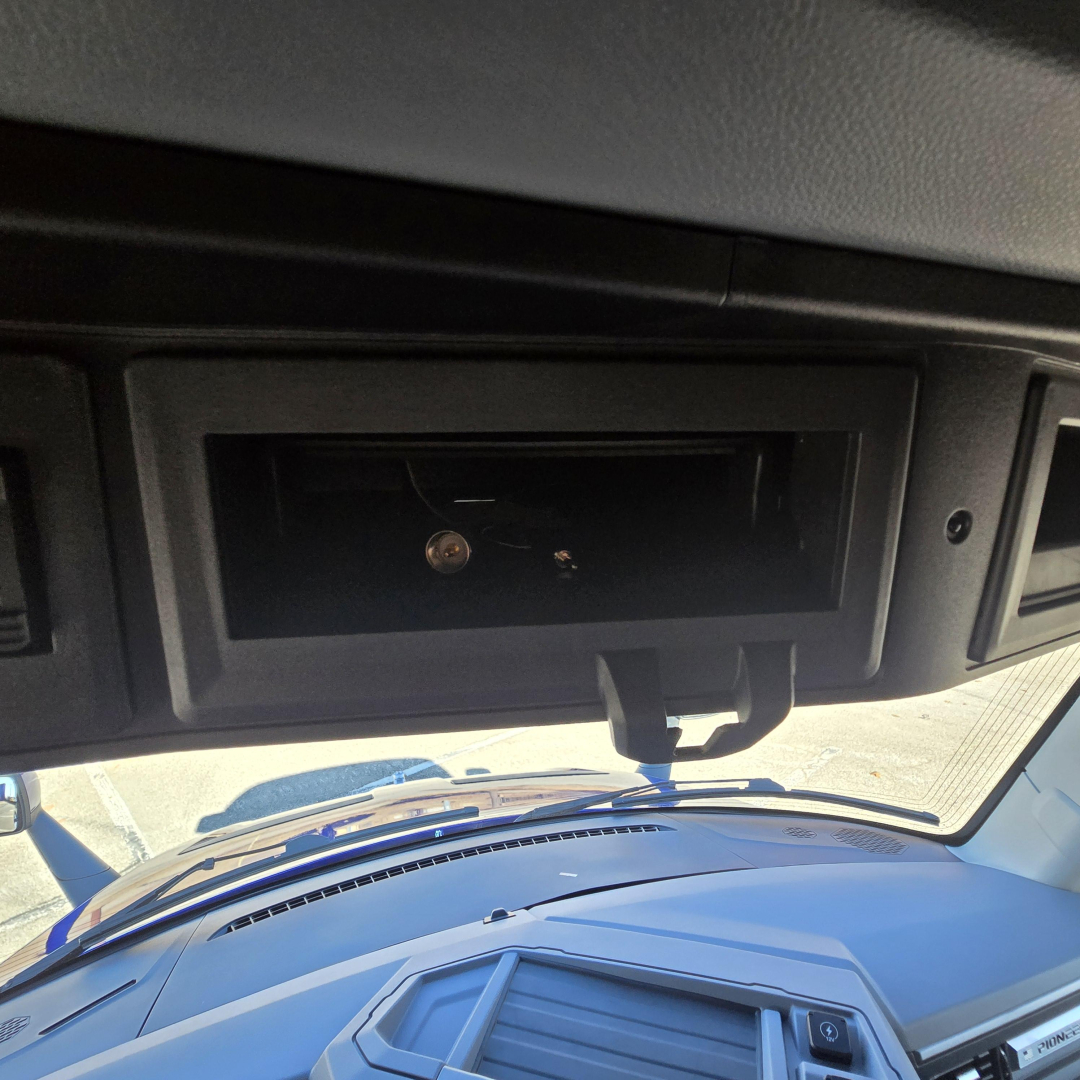Truck dash area showing an empty storage slot or compartment under the dash with a small latch visible, windshield and hood seen through the front.