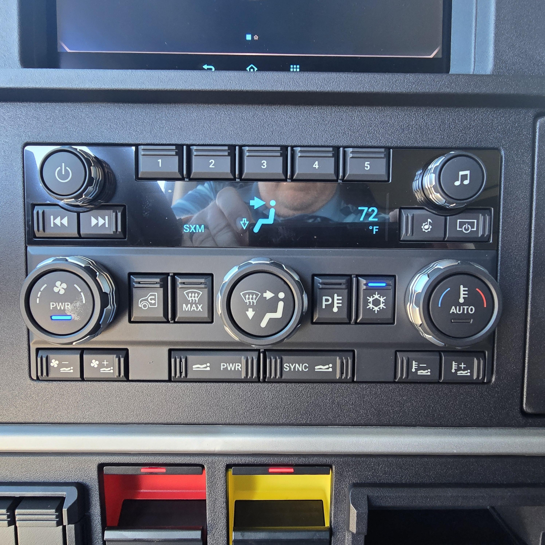Dashboard controls of a 2026 Mack PR64T76H showing climate and media controls, knobs, and labeled buttons.