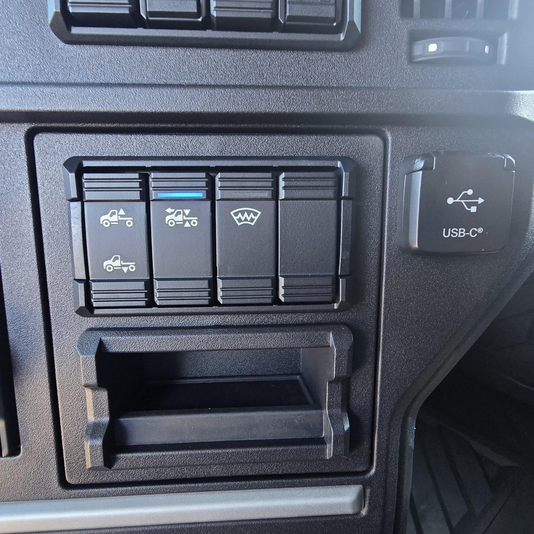 Dashboard controls panel with four labeled switches and icon indicators, plus a small USB-C port cover to the right; navigation slot below.