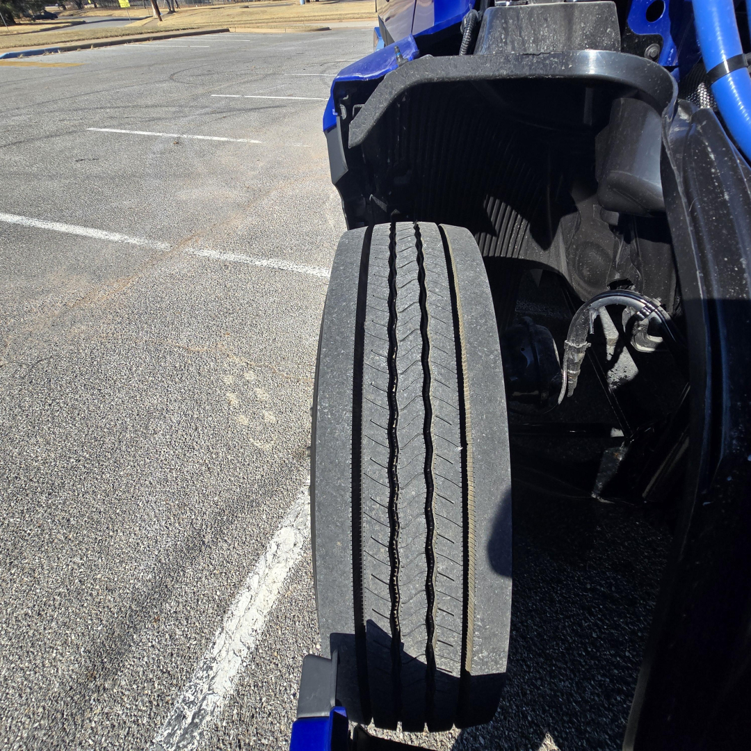 Front left dual-tire setup of a blue Mack PR64T76H truck showing a large steer axle tire with tread pattern and surrounding components