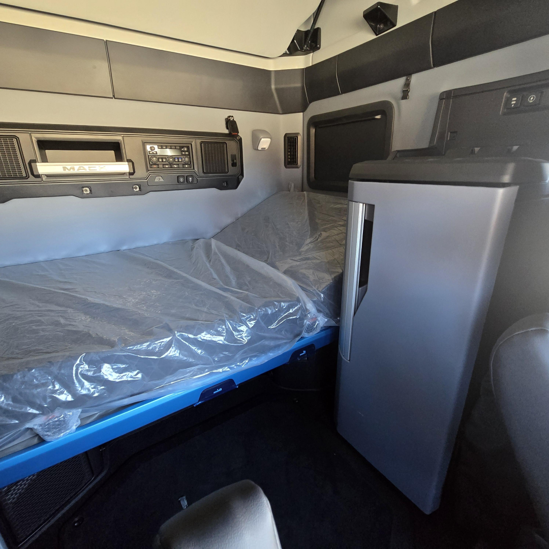 Interior sleeper cab of a 2026 Mack PR64T76H truck showing a bunk bed with plastic-covered mattress, side cabinet, and dashboard controls.