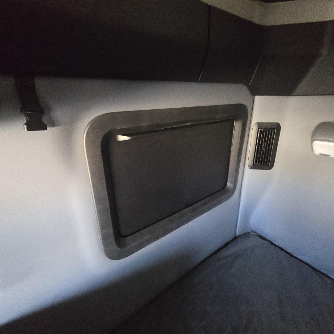Interior side panel in a Mack PR64T76H sleeper cab showing a recessed storage hatch and a small vent, with a carpeted floor edge.