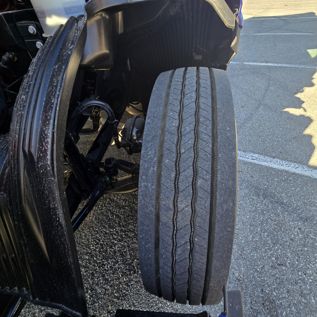 Truck wheel and tire tread close-up view in Mack PR64T76H cab area showing front duals and suspension.