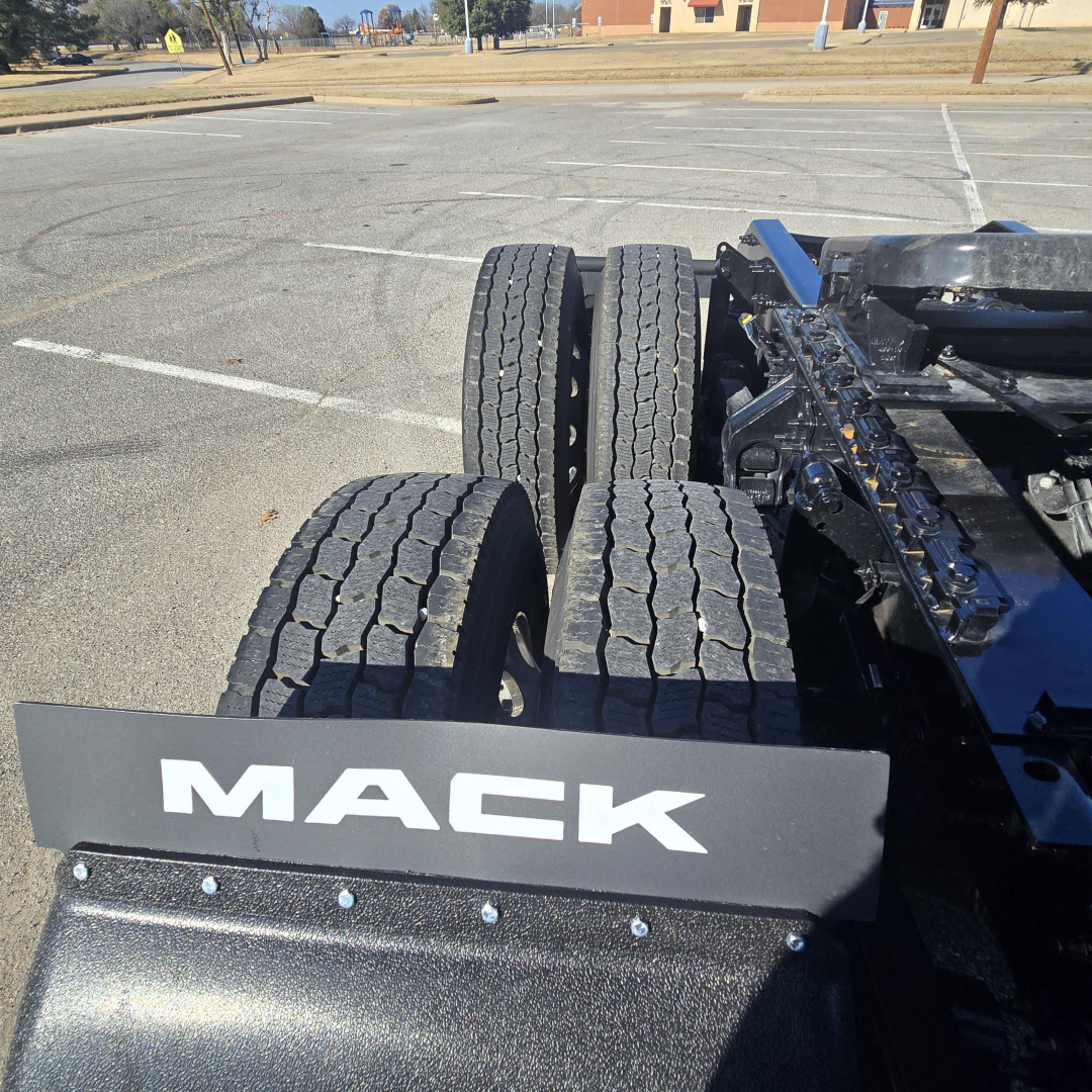 Mack tractor rear dual wheels and fender showing MACK logo on mudguard. Part of long-haul truck chassis with tires and blue frame visible.