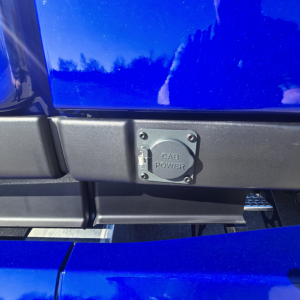 Cab power inlet cover on blue Mack PR64T76H truck showing square plug cover with bolts
