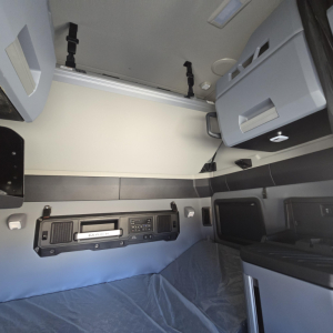 Cabin interior of Mack PR64T76H truck showing dashboard radio and control panel, bunk area, and overhead storage compartments in a sleeper (no data not visible).